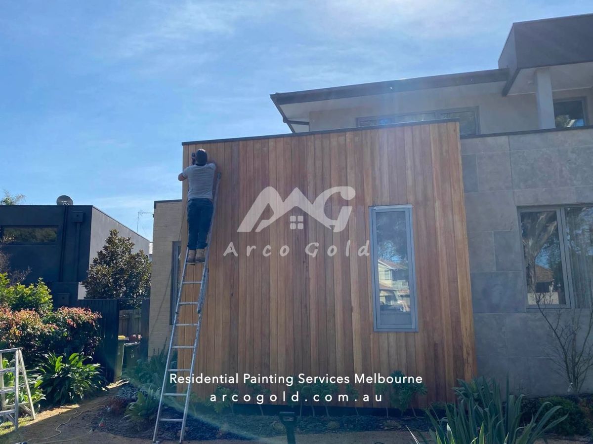 Timber-clad house facade mid-repaint with ladder in place